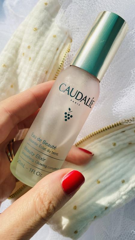 Hand holding a Caudalie skincare bottle with a blurred background