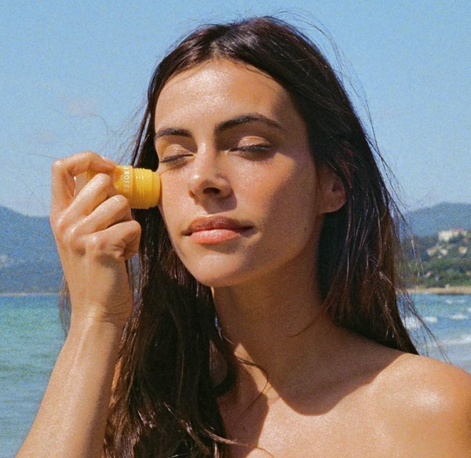 Woman applying sunscreen on her face with a beach in the background