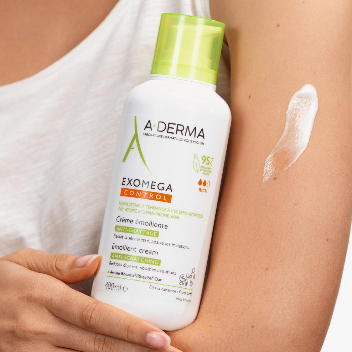 A-Derma Exomega Control, woman holding the pump bottle beside a cream swatch on her arm