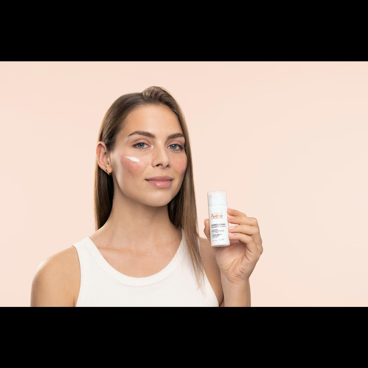 Avène Antirougeurs Rosamed, woman holding the pump bottle with a cream dab on her cheek