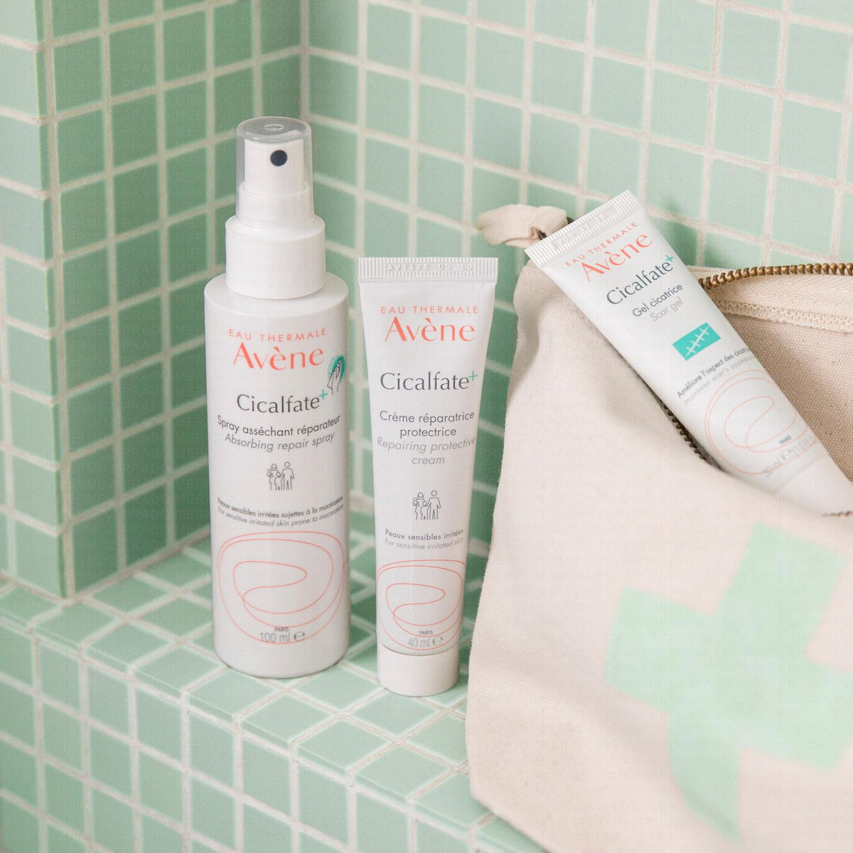 Avène Cicalfate+, spray bottle and two tubes with a pouch on green tiles