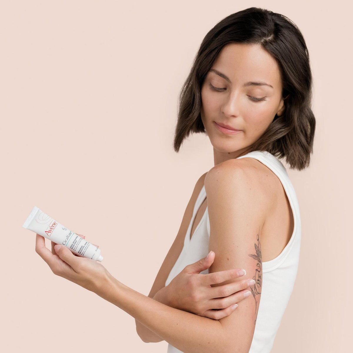 Avène Cicalfate, woman holding the tube with a hand on her tattooed arm