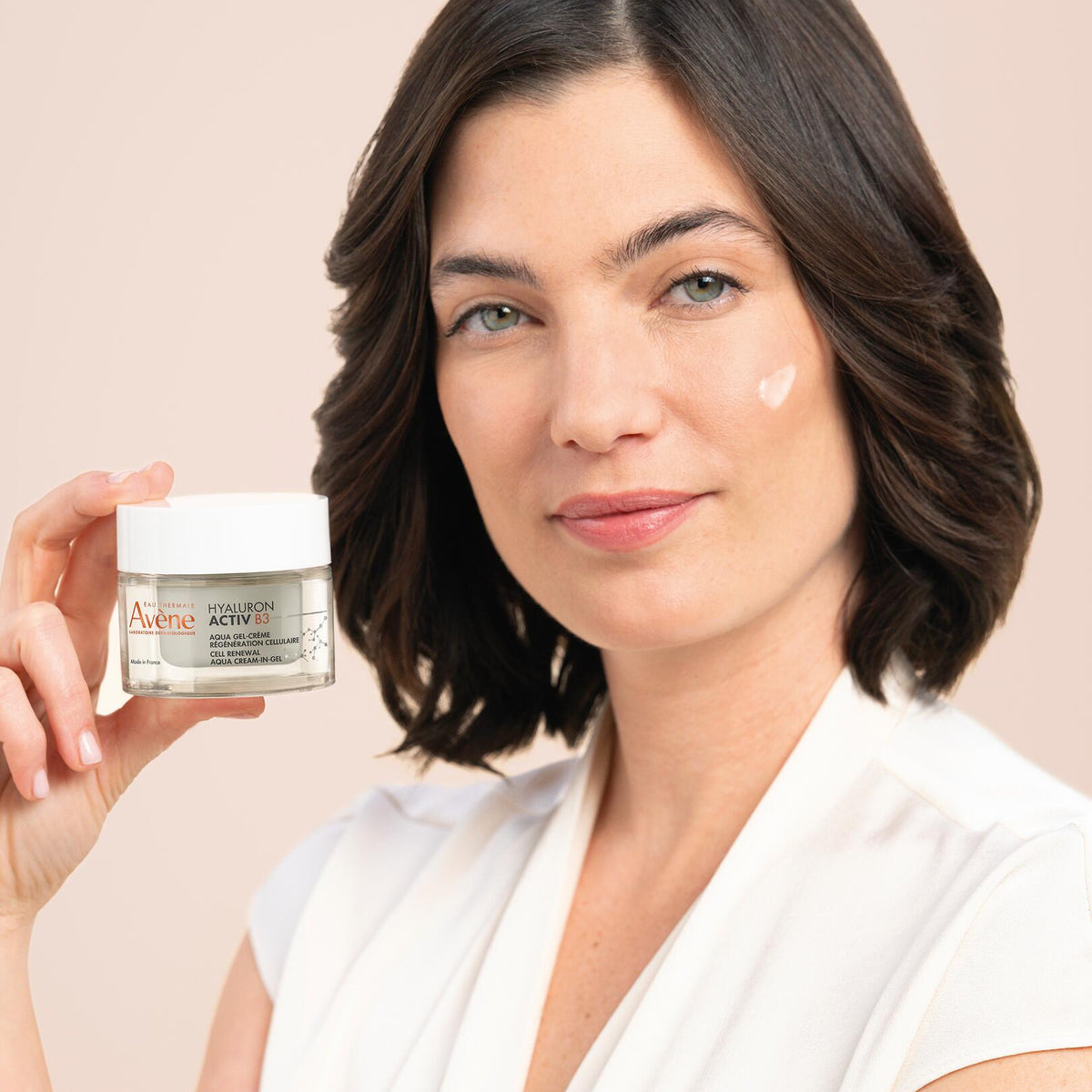 Avène Hyaluron Activ B3, woman holding the jar with a dab of cream on her cheek