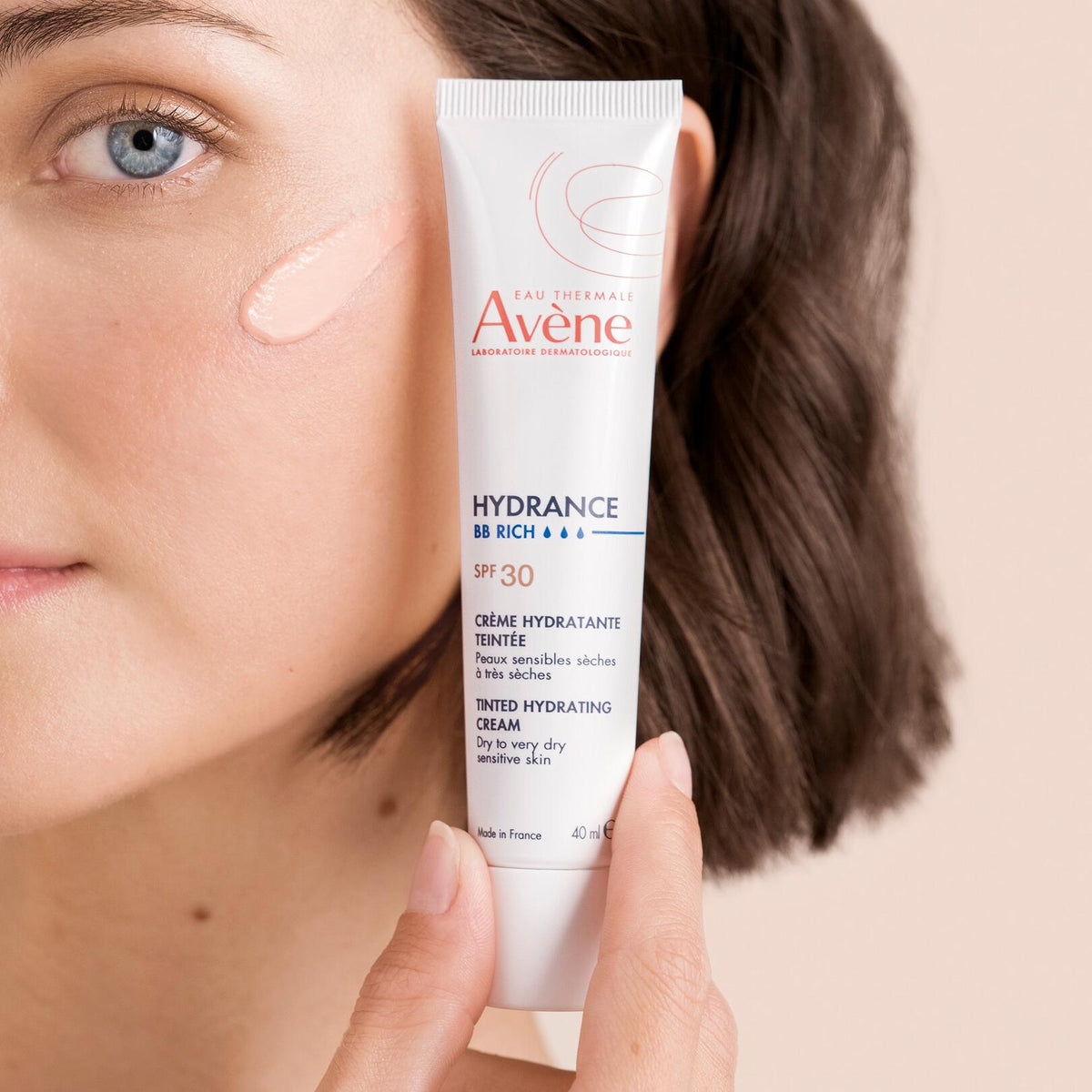 Avène Hydrance, woman holding the tube beside a cream swatch on her cheek