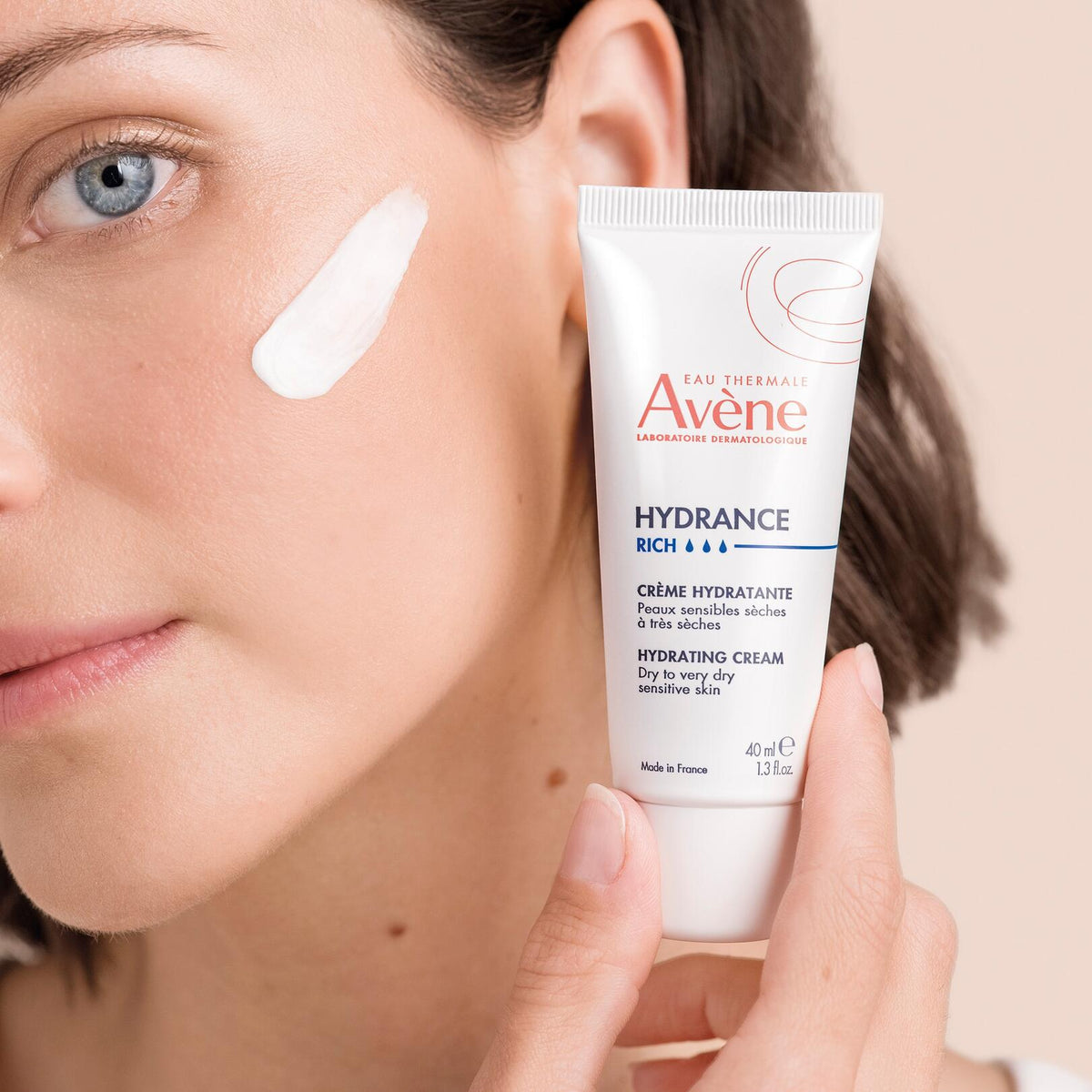 Avène Hydrance, woman holding the tube beside a cream swatch on her cheek