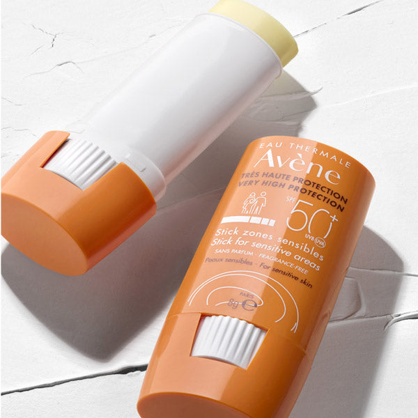 Avène Solaire, two sticks, one with the cap off, on a white textured surface
