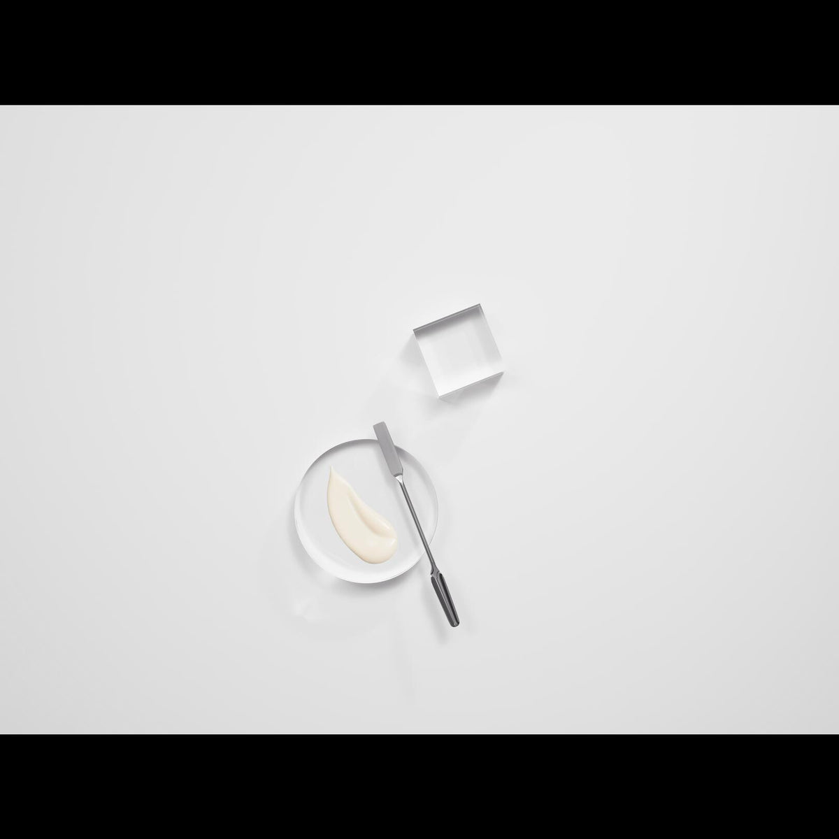 Avène Solaire, fluid swatch on a glass dish with a spatula, black bands