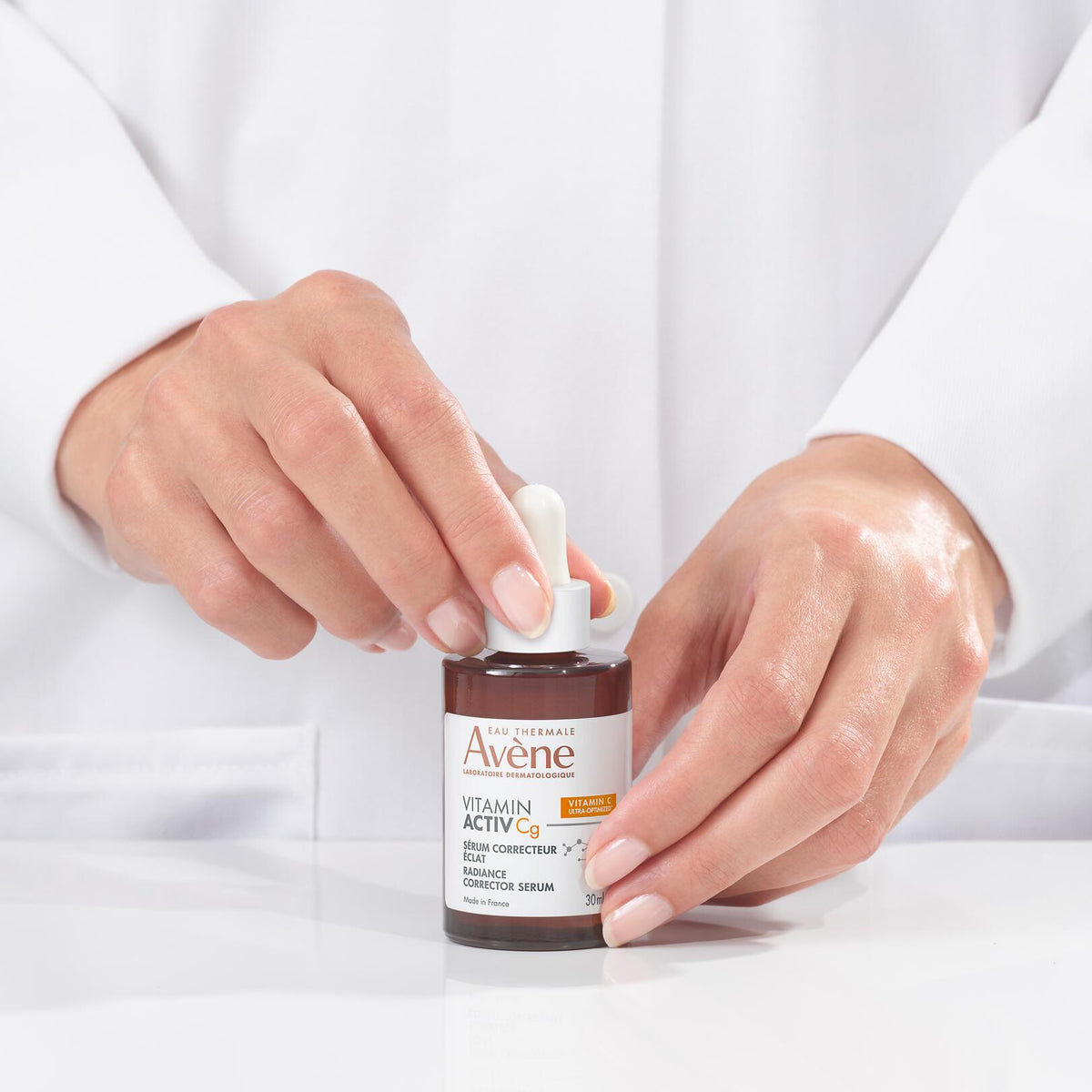 Avène Vitamin Activ Cg, hands in a lab coat opening the glass bottle