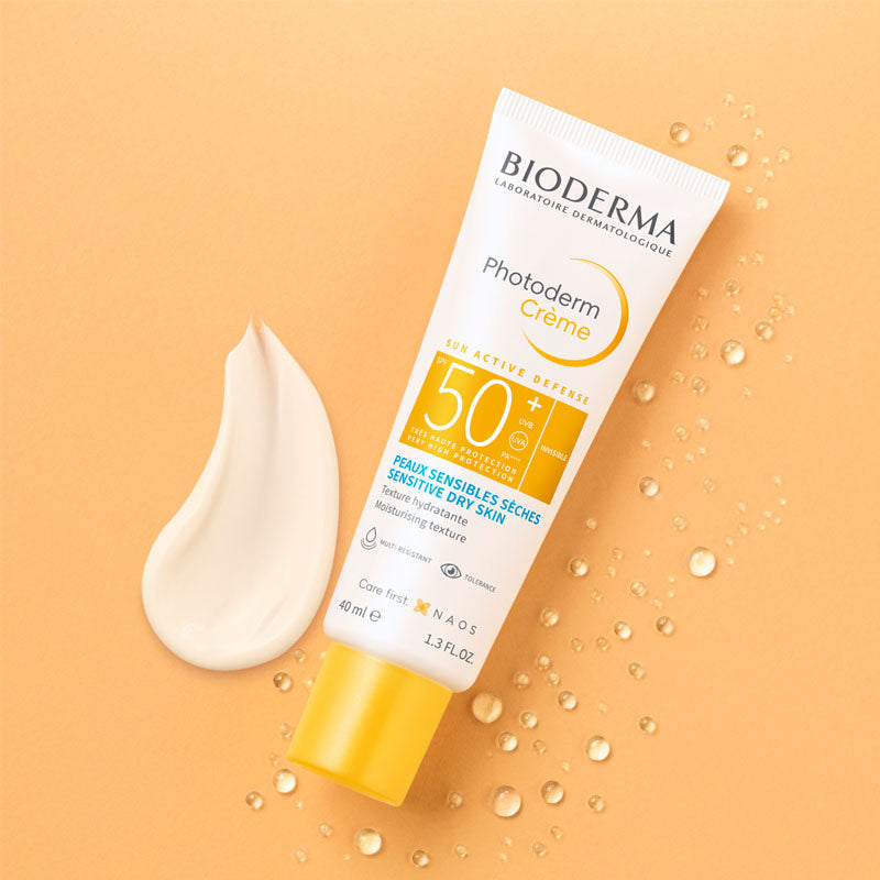 Bioderma Photoderm, tube and cream swatch on a peach background with droplets