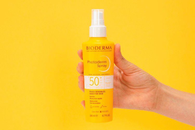Bioderma Photoderm, hand holding the spray bottle in the old packaging on a yellow background