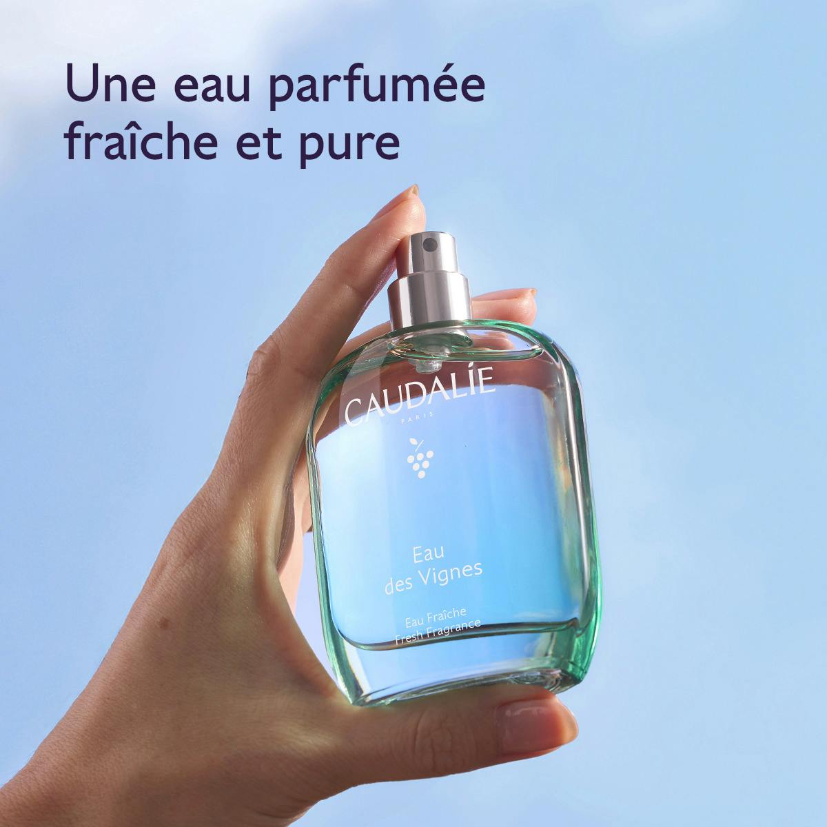 Caudalie Eau des Vignes, hand holding the bottle against a blue sky, text in French