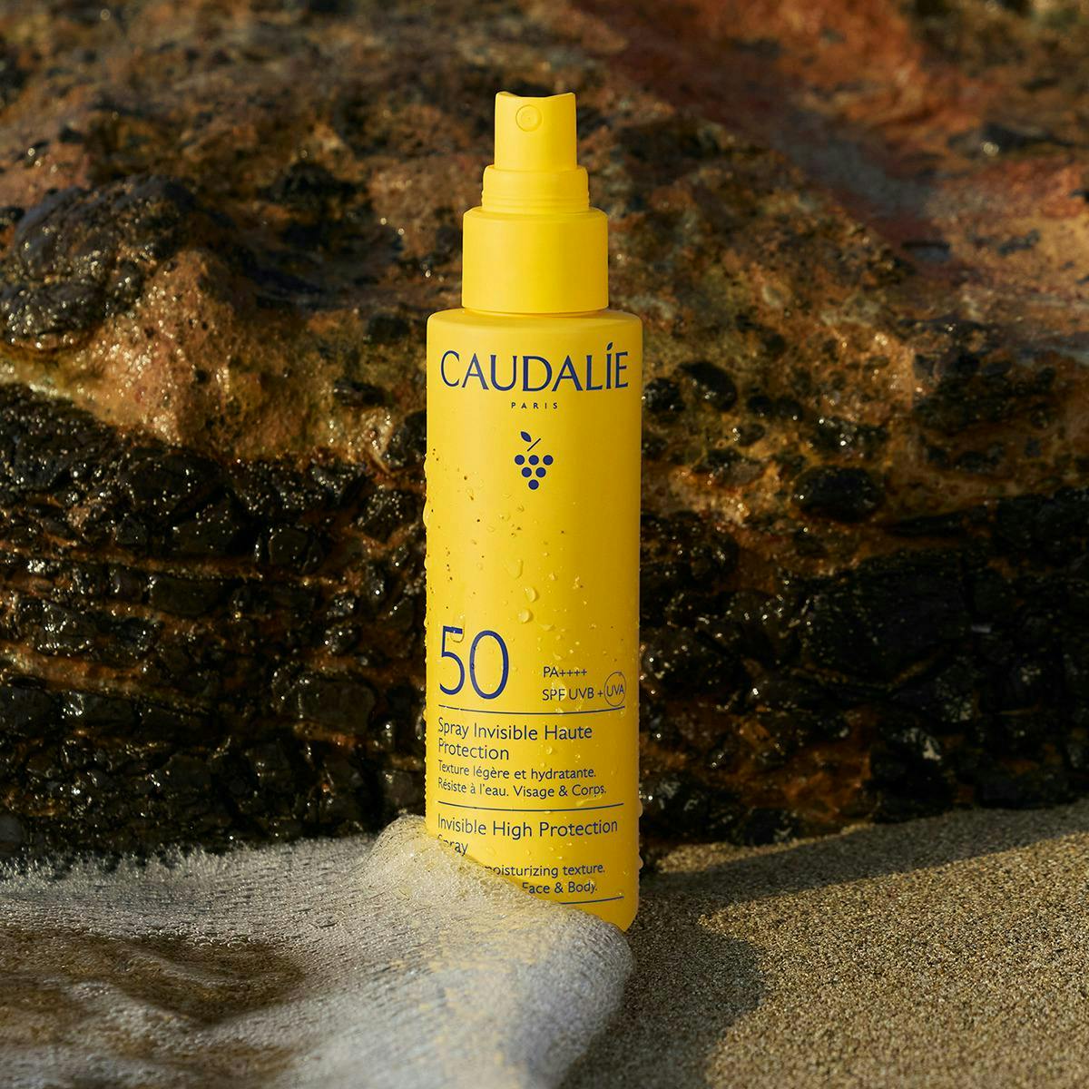 Caudalie Milky Sun Spray, spray bottle on a wet rock by the sea