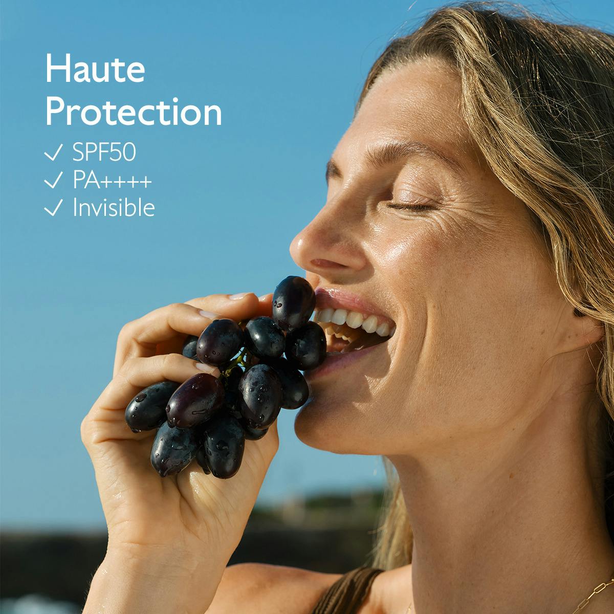 Caudalie Milky Sun Spray, woman biting into black grapes by the sea
