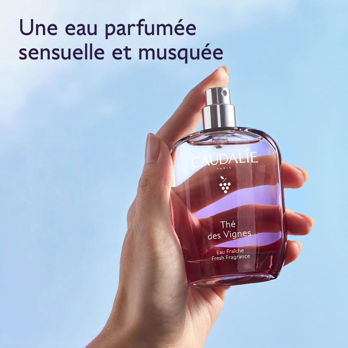 Caudalie Thé des Vignes, hand holding the glass bottle against a blue sky