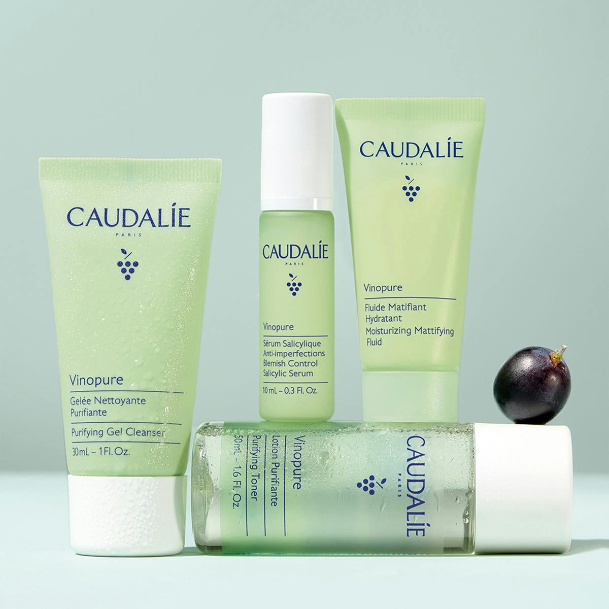 Caudalie Vinopure, four travel-size products stacked with a dark grape