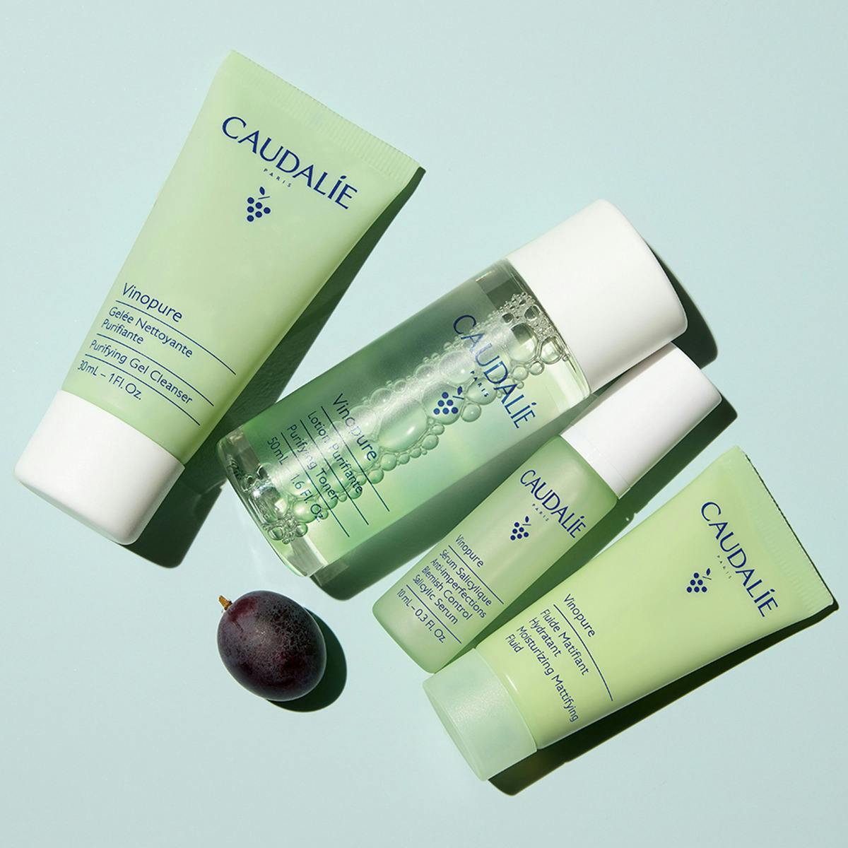 Caudalie Vinopure, four travel-size products laid flat with a dark grape