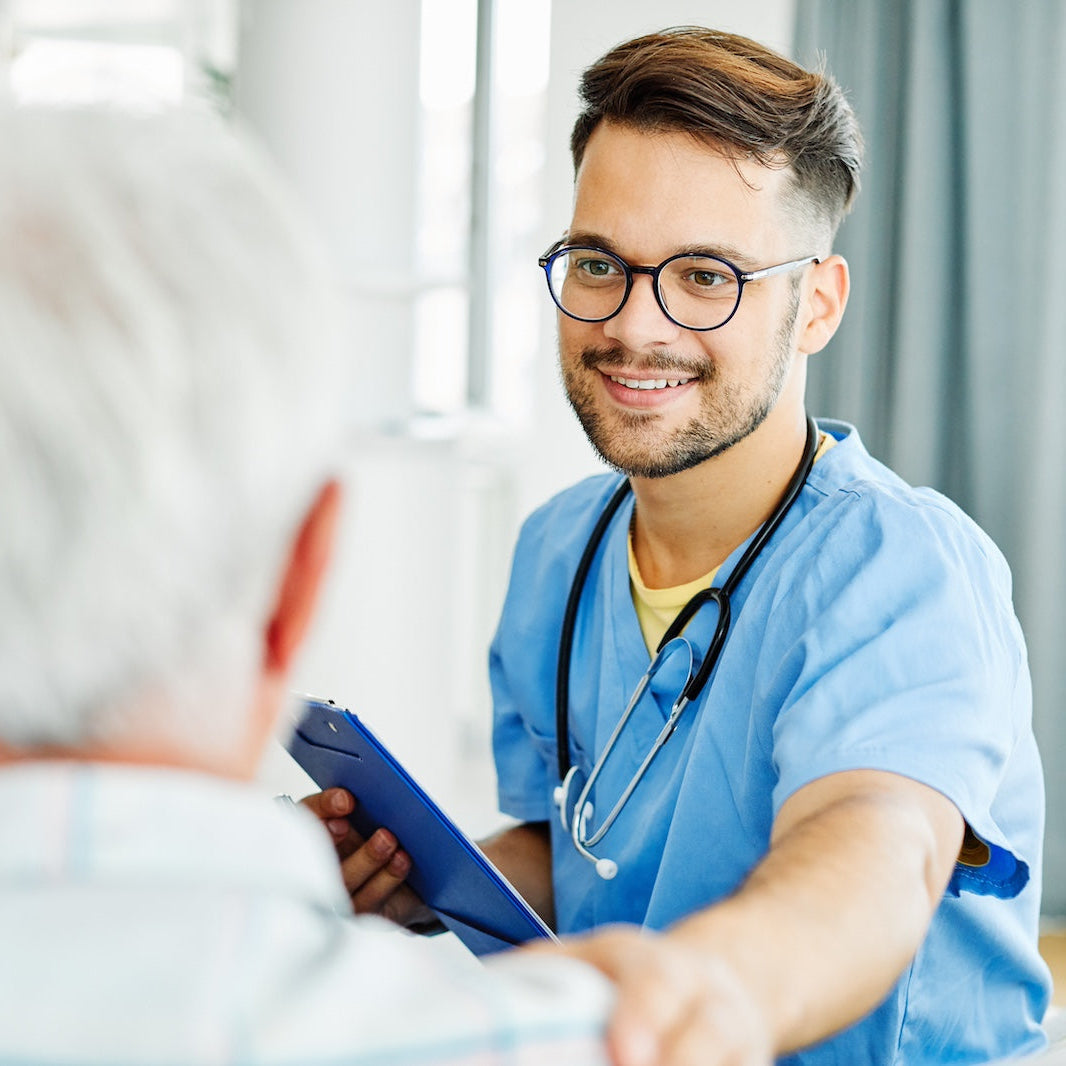 Doctor in blue scrubs with a tablet interacting with a patient in a medical setting.