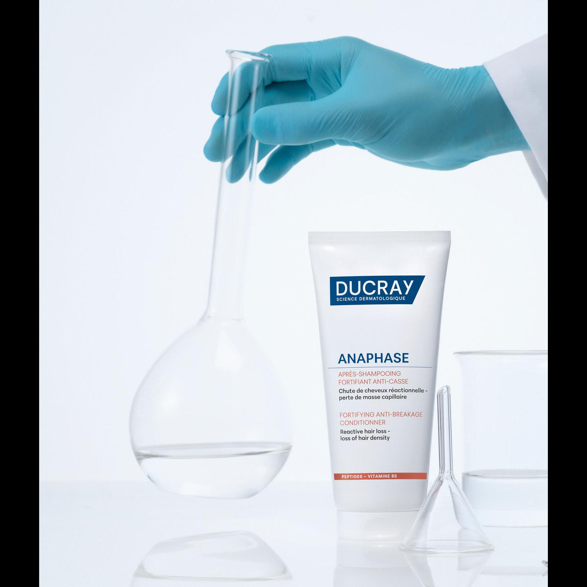 Ducray Anaphase+, tube next to laboratory glassware and a gloved hand