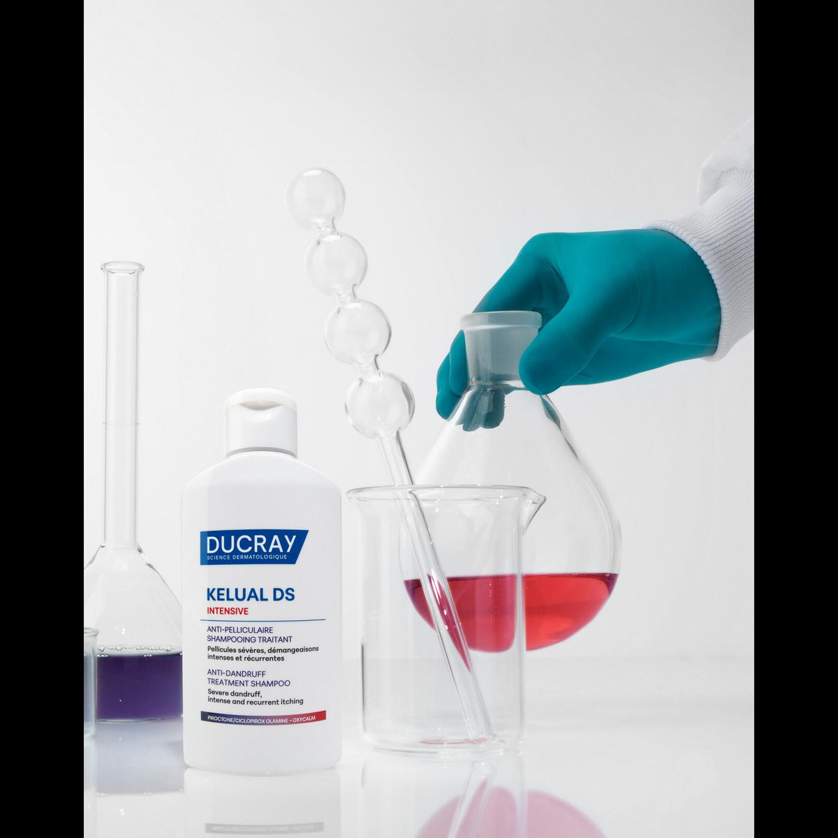 Ducray Kelual DS, bottle next to laboratory glassware and a gloved hand