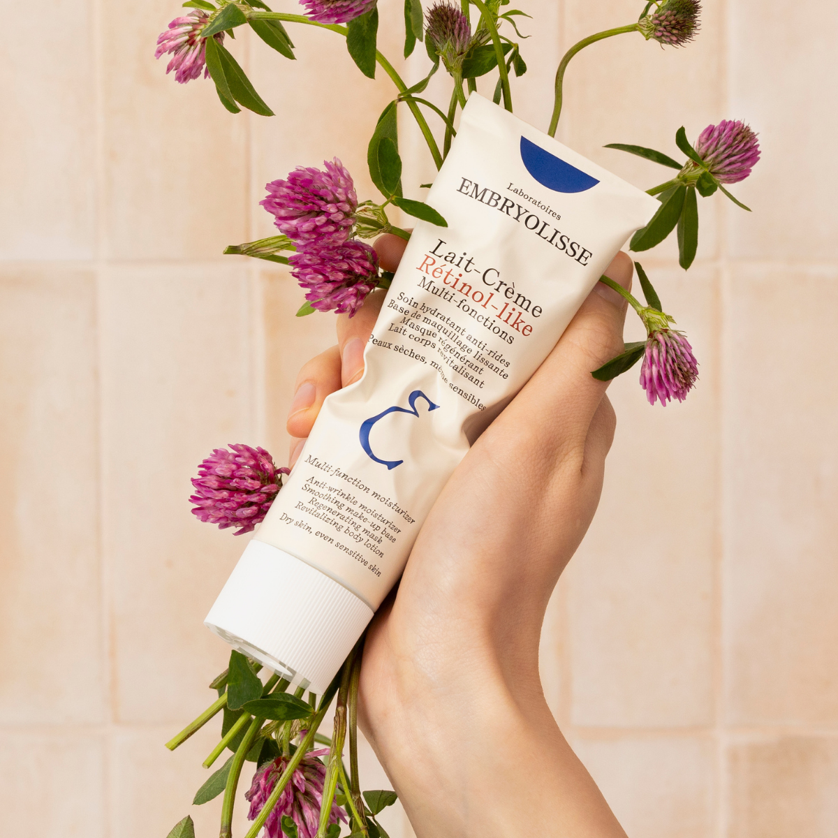 Embryolisse Retinol-Like Cream Milk, hand holding the tube among pink clover flowers