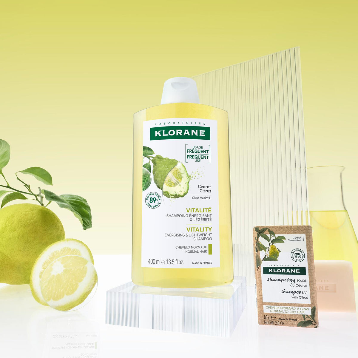Klorane Citron, bottle and solid shampoo bar with citrons on a yellow background