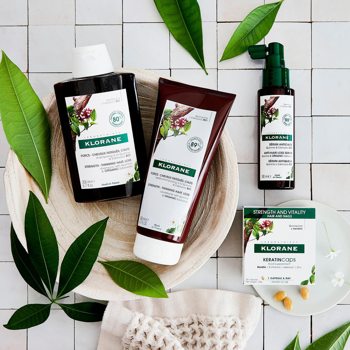 Klorane KeratinCaps, box and capsules beside quinine hair care products on white tiles