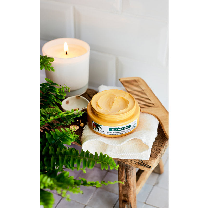Klorane Mango, open jar on a wooden stool with a candle and fern