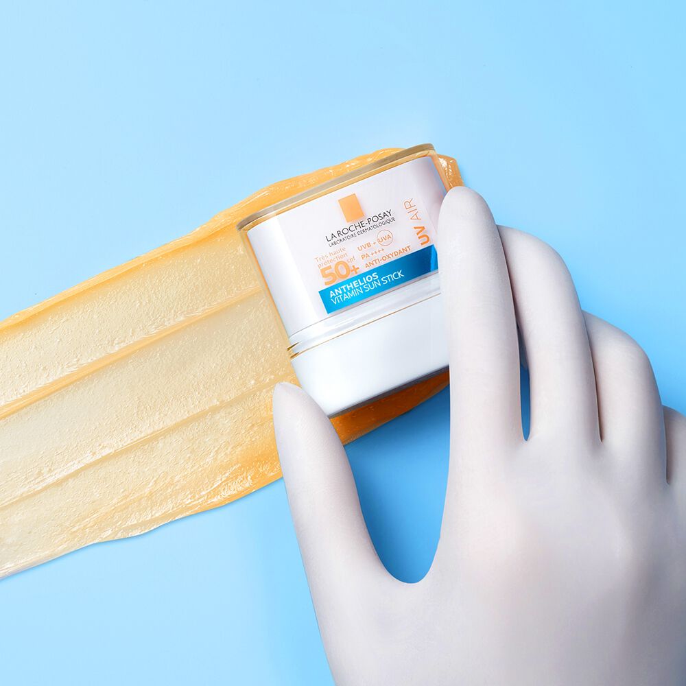 La Roche-Posay Anthelios, gloved hand holding the stick over a balm swatch
