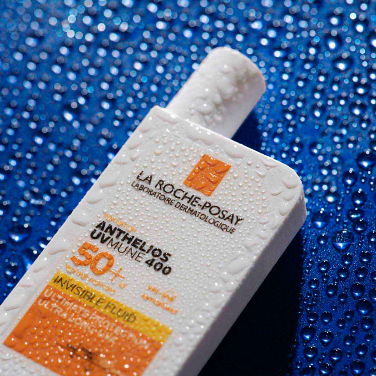 La Roche-Posay Anthelios UVMune 400 Invisible Fluid SPF 50+ bottle covered in water droplets on a blue background