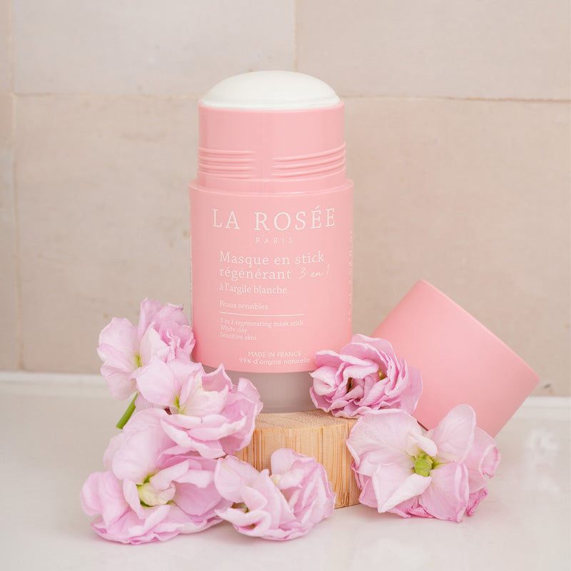 La Rosée Regenerating Mask Stick, open stick and cap among pink flowers