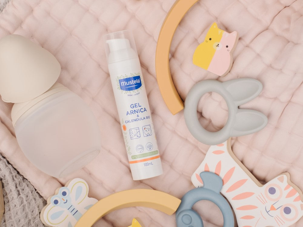 Mustela Arnica and Calendula Gel, bottle among baby toys on a pink quilt