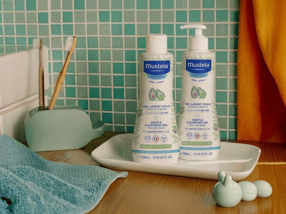 Mustela Body and Hair Wash, bottle and pump bottle on a tray by blue tiles