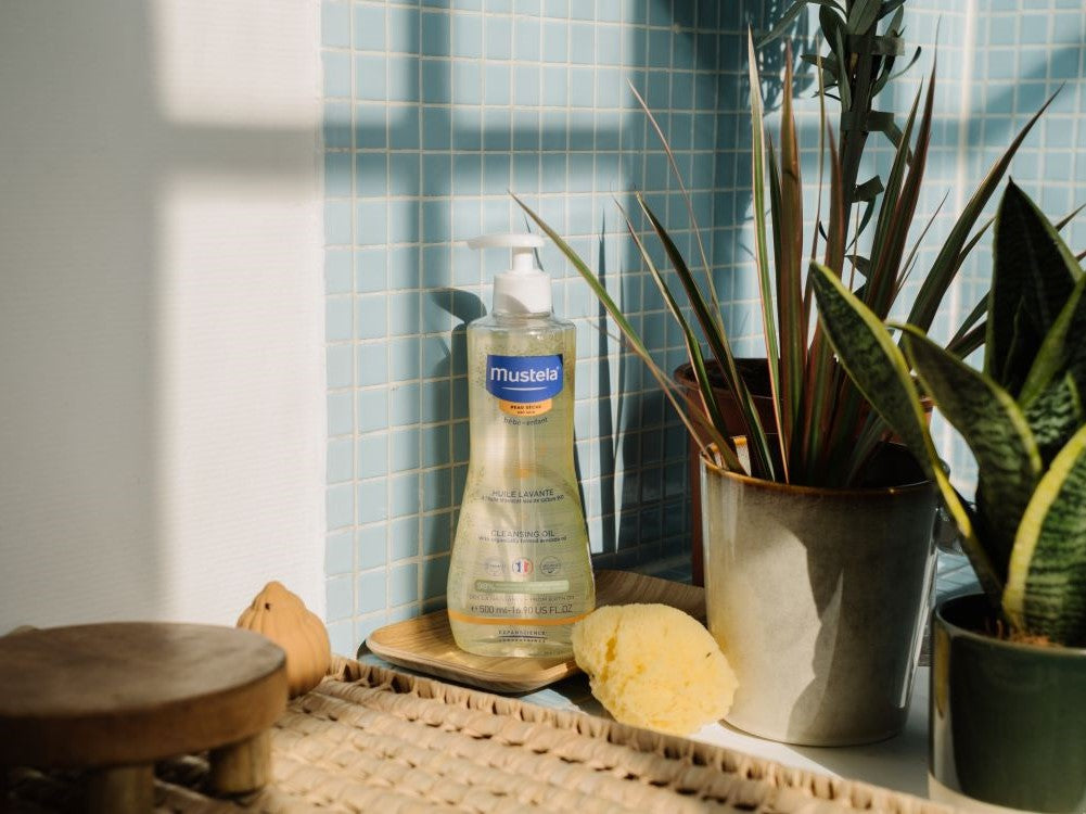 Mustela Cleansing Oil, pump bottle with a sponge and plants on a bathroom shelf
