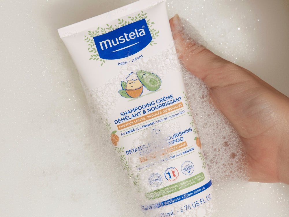 Mustela Detangling Cream Shampoo, hand holding the tube in bath foam