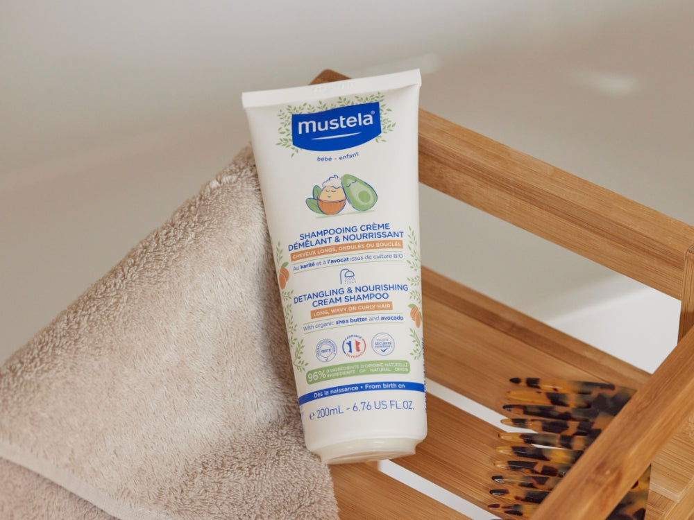 Mustela Detangling Cream Shampoo, tube on a wooden bath rack with a towel and comb