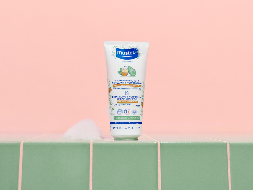 Mustela Detangling Cream Shampoo, tube on green tiles against a pink wall