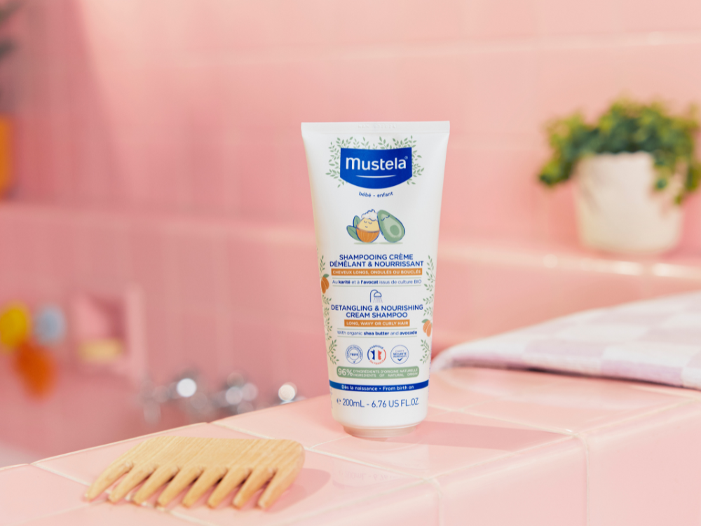 Mustela Detangling Cream Shampoo, tube on a pink-tiled bath edge with a wooden comb