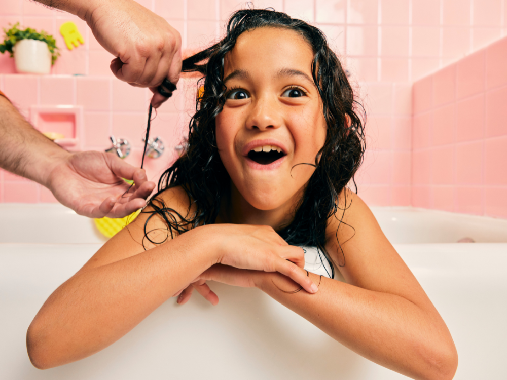 Mustela Detangling Cream Shampoo, adult combing a laughing girl's curly hair in the bath