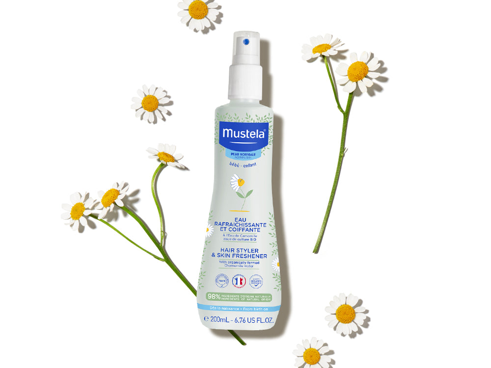 Mustela Refreshing and Styling Water, spray bottle among chamomile flowers