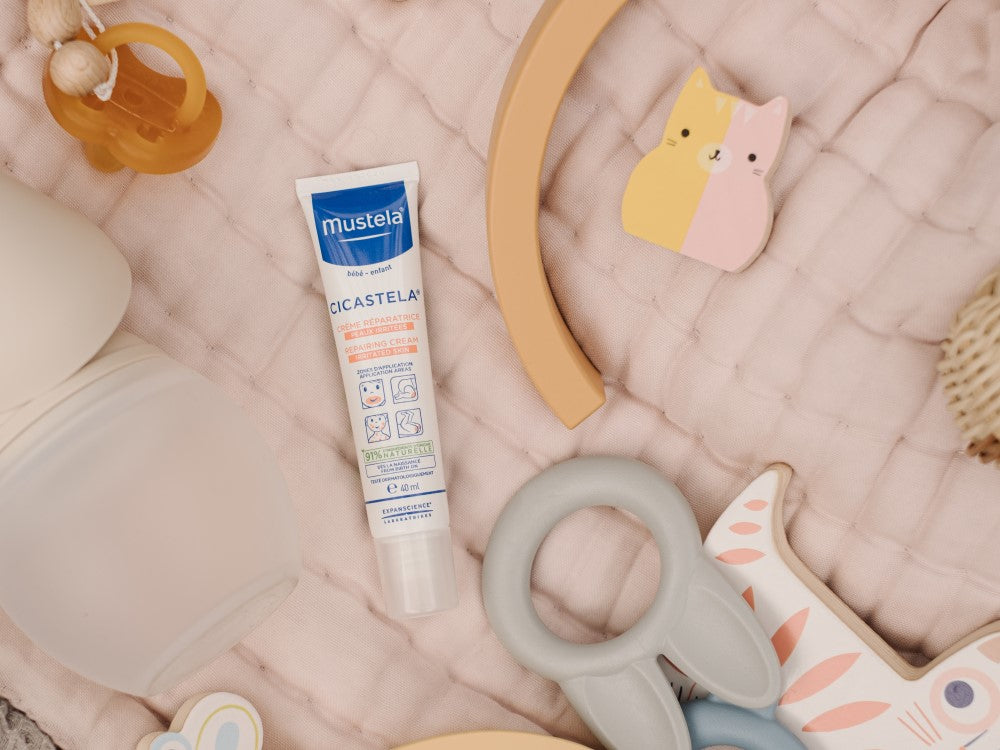 Mustela Cicastela, tube on a pink quilted blanket among baby toys