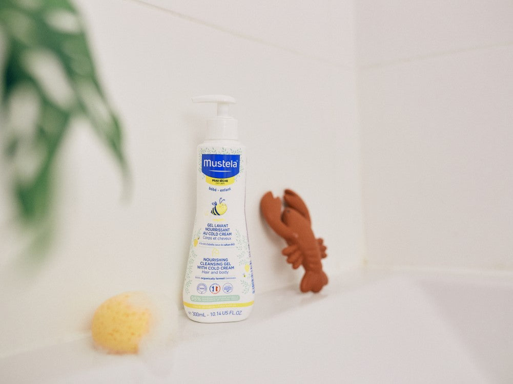 Mustela Cold Cream, pump bottle on a bathtub edge with a sponge and a toy