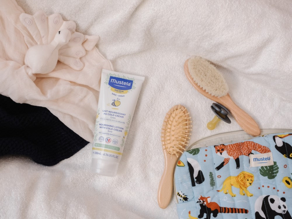 Mustela Cold Cream, tube on a towel with baby brushes and a printed pouch