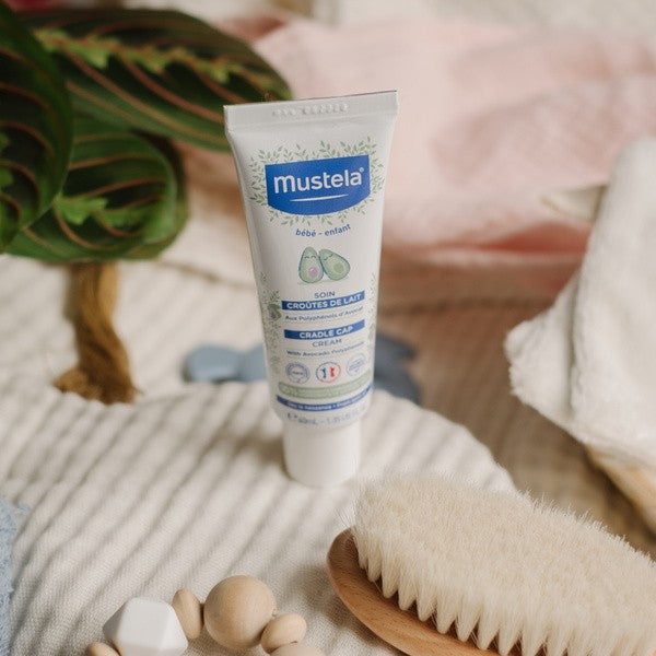 Mustela Cradle Cap Cream for Babies, tube on a knit blanket with a wooden baby brush