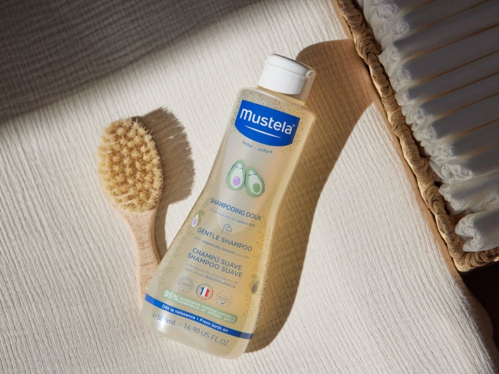 Mustela Gentle Shampoo, bottle with a baby brush on a white cloth