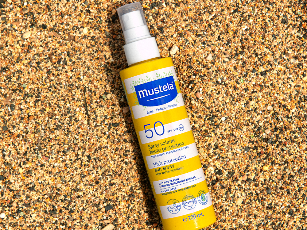 Mustela Sun Spray SPF 50, spray bottle lying on sand