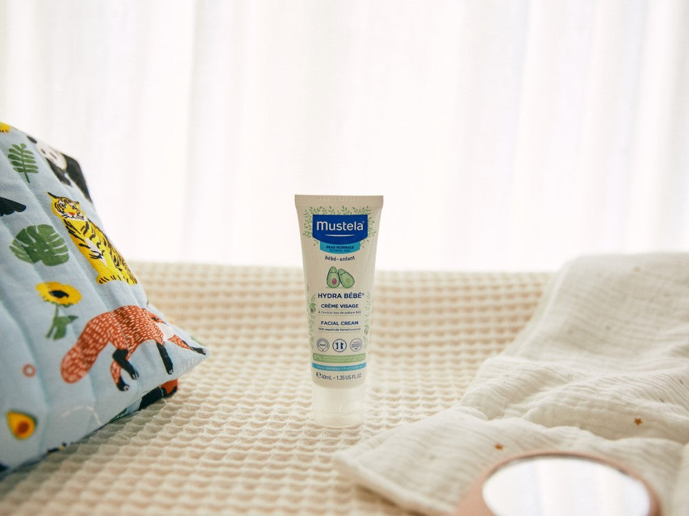 Mustela Hydra Bébé, tube on a knit blanket beside a printed pouch