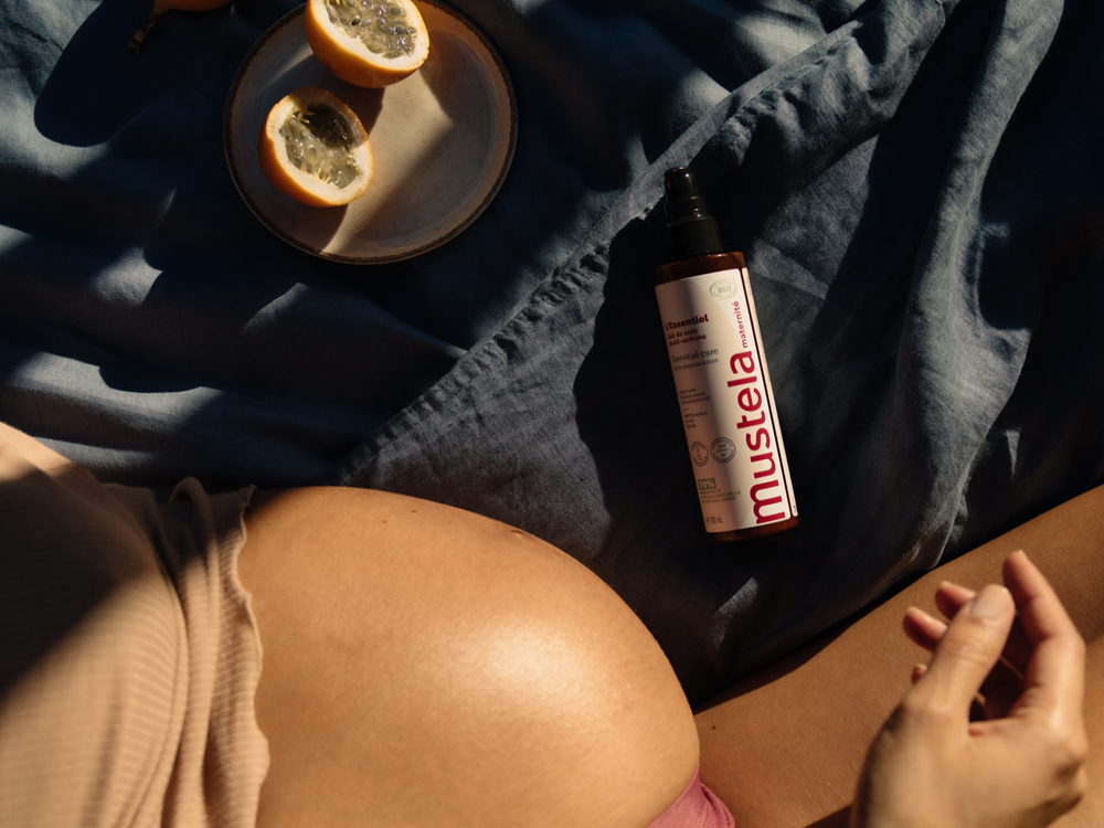 Mustela Multi-Action Milk, bottle beside a woman's bare belly and passion fruit