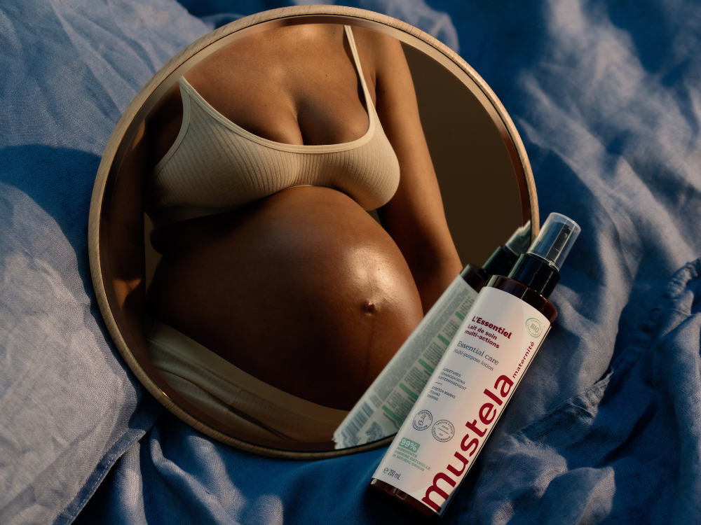 Mustela Multi-Action Milk, bottle on a round mirror reflecting a woman's belly