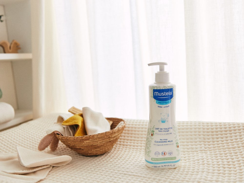 Mustela No-Rinse Cleansing Milk, pump bottle on a changing mat beside a basket of cloths