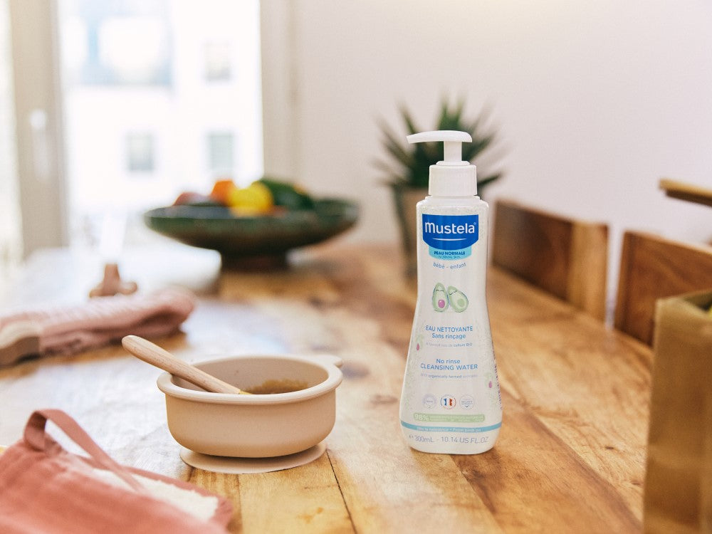 Mustela No-Rinse Cleansing Water, pump bottle on a wooden table beside a baby bowl